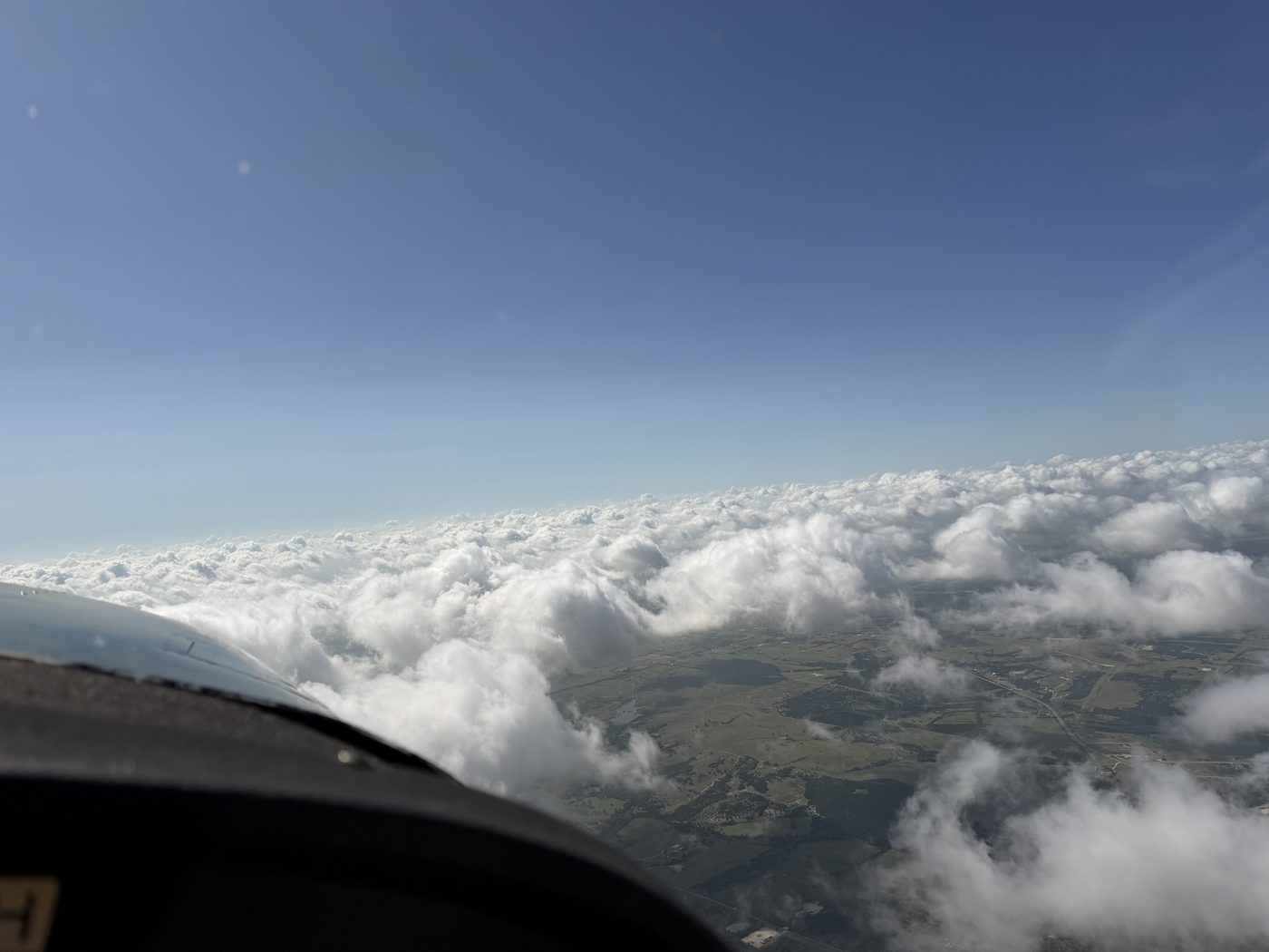 View from the cockpit above a layer of cumulus clouds over the Texas countryside
