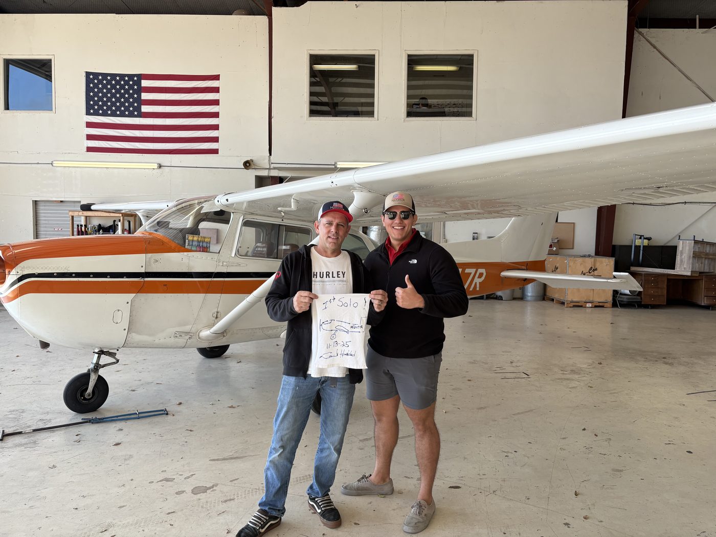 Student holding his first solo shirt in the hangar beside Cessna 172 N5247R